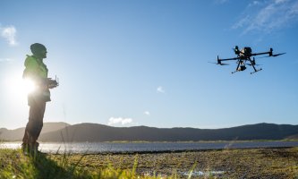 En mann som styrer end rone i luften ved et vann. Foto: Trygve Heide/NIVA.