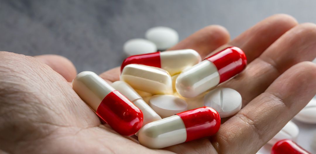 A hand holds an array of capsules and pills
