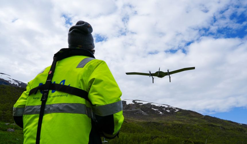 A NIVA employee flies a drone and there's a blue sky and clouds beyond.