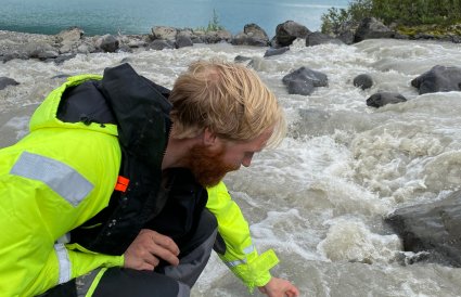 Mann tar vannprøver i et elveutløp.